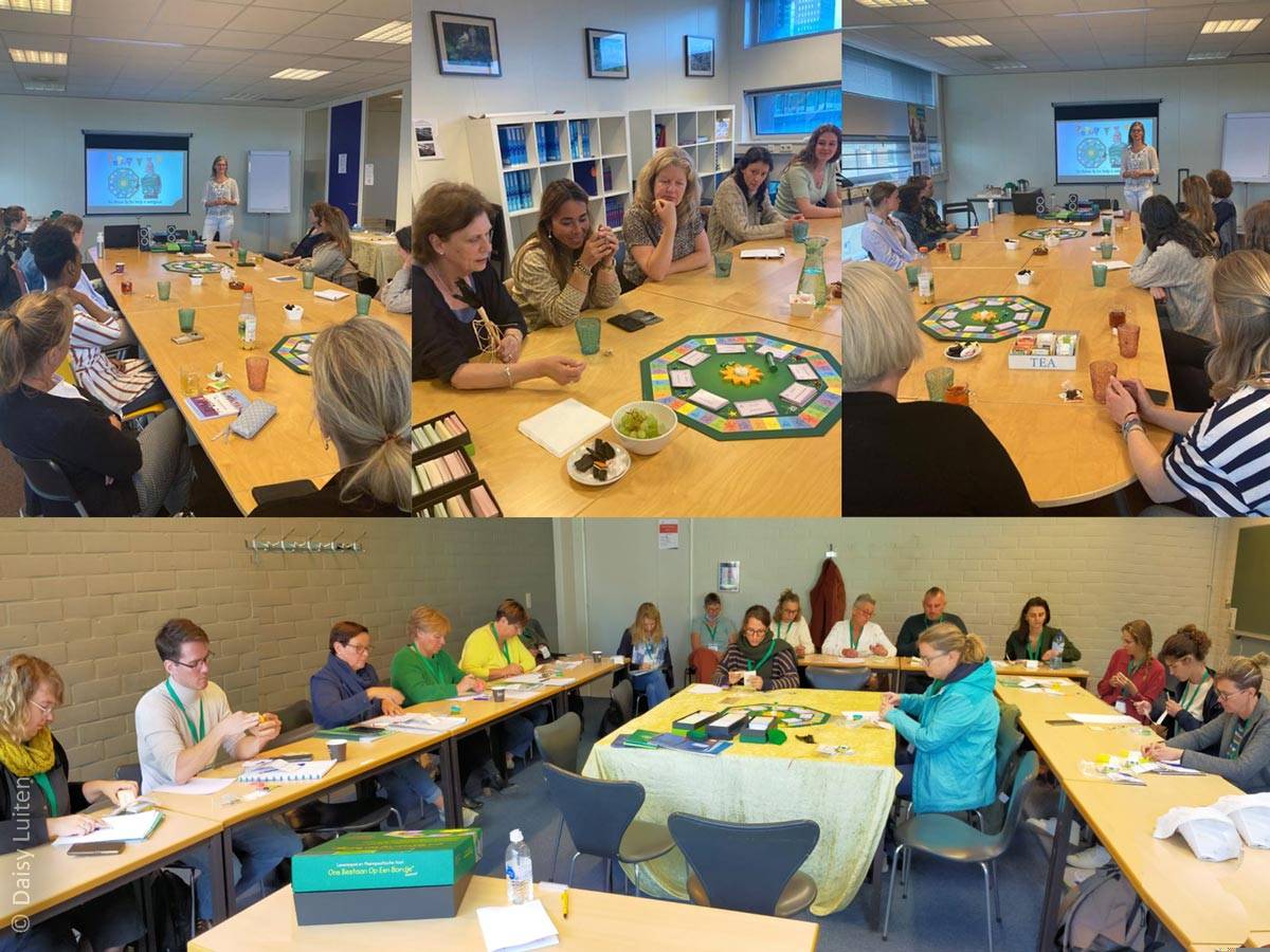 Daisy Luiten presenteert haar spel tijdens een workshop voor een groep mensen. In het midden van de ruime groep ligt Ons Bestaan Op Een Bordje op tafel. Ook wordt de tool gespeeld met de groep.