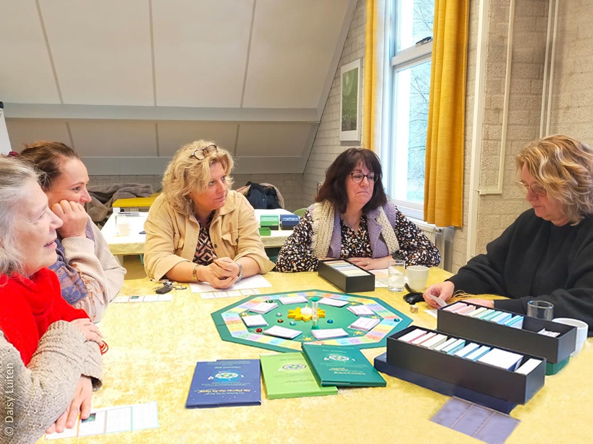 Deelnemers van de training werken met Ons Bestaan Op Een Bordje zitten aan tafel rond dit groene kleurrijke achthoekige therapeutische bordspel. Daisy Luiten leert therapeuten en coaches hoe ze met deze tool kunnen werken.