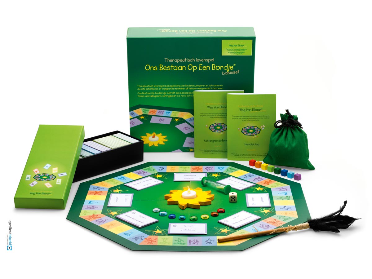 De therapeutische tool Ons Bestaan Op Een Bordje, in de vorm van een 8-hoekig donkergroen bordspel van Daisy Luiten staat uitgestald, met pionnen in de vorm van tranen, een praatstok en een houten zonnetje met lichtje in het midden.